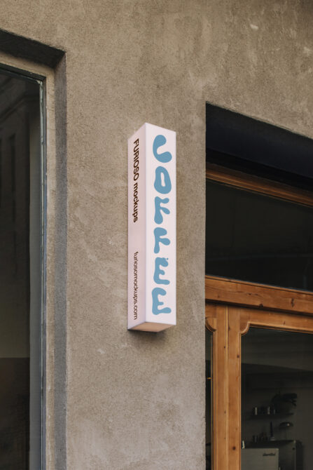 Vertical white box sign with blue rounded letters reading coffee mounted on concrete