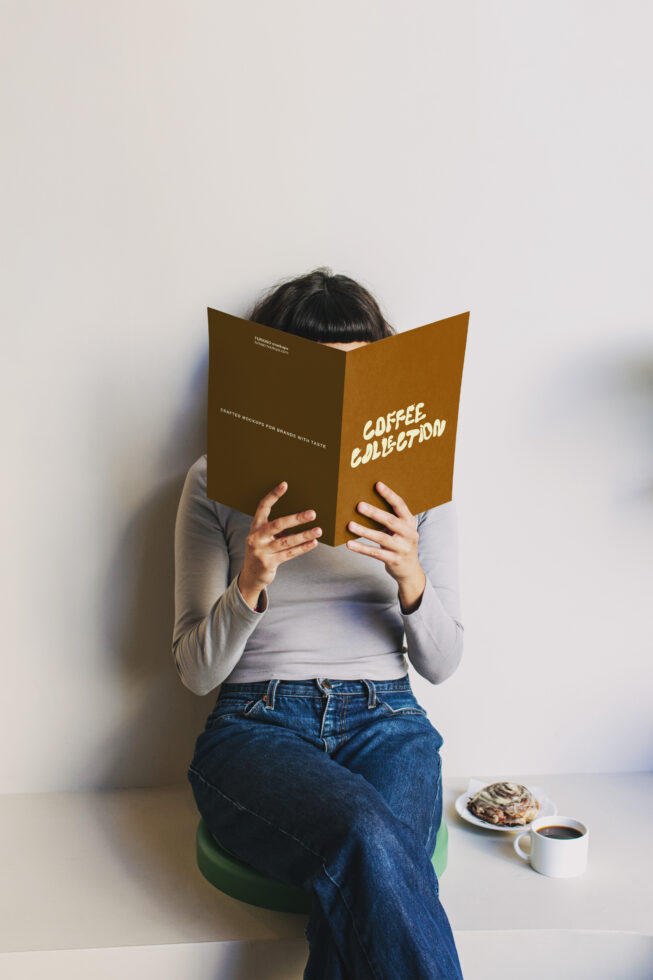 Seated person reading gold book, cookie crumbs on plate with coffee cup nearby