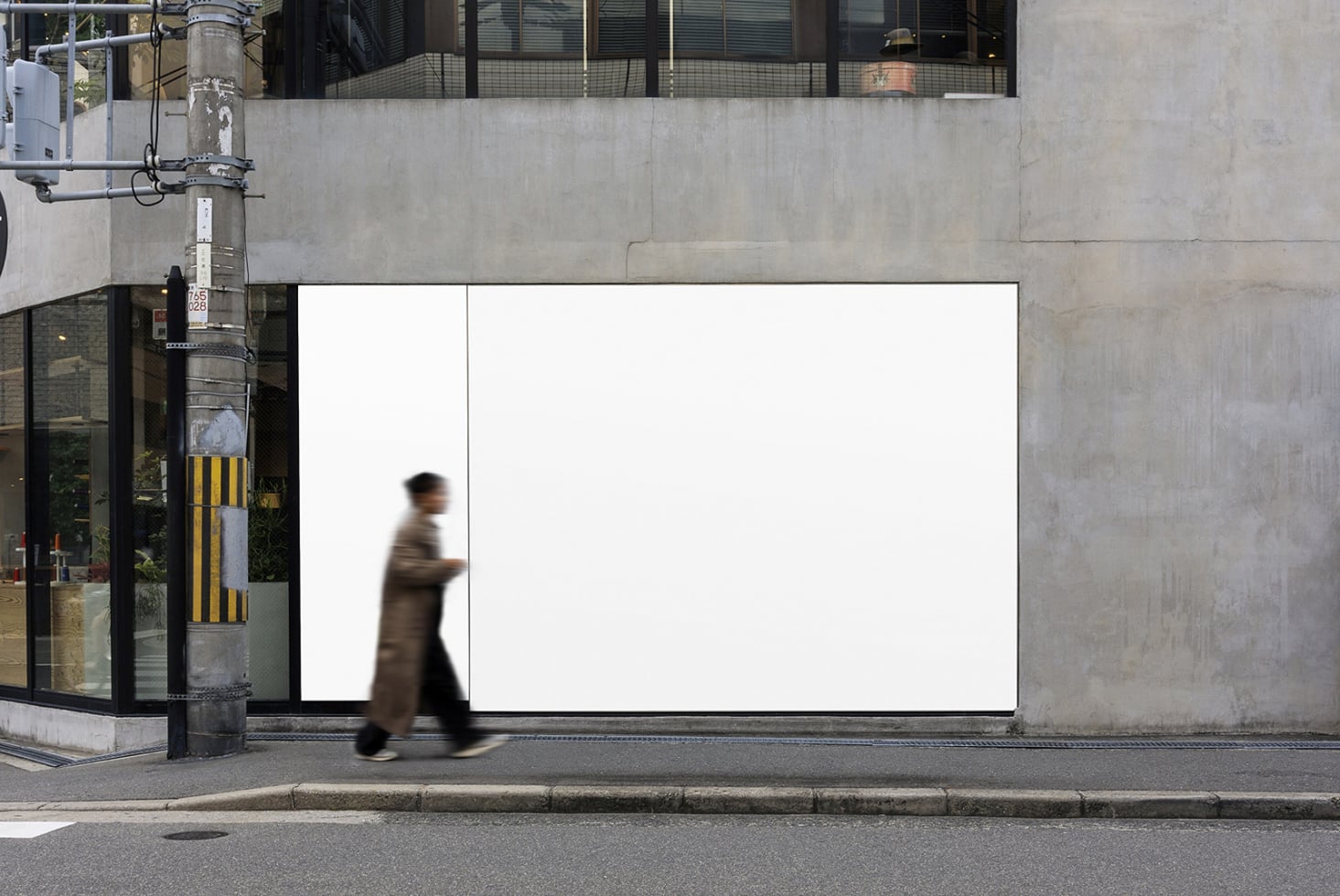 Blank white billboard on urban storefront with blurred person walking past concrete building