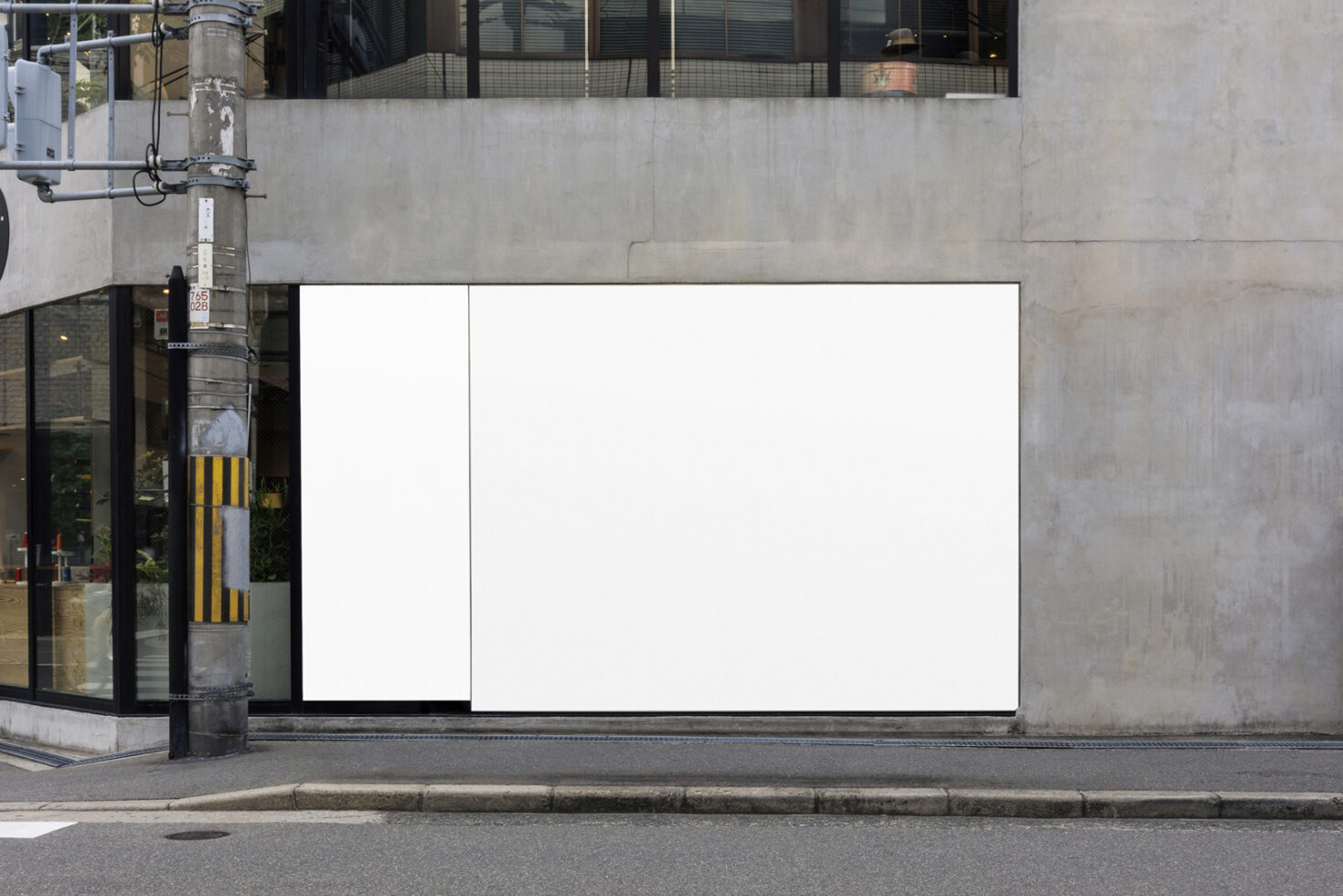 Blank storefront billboard mockup on urban street with concrete wall, metal pole, storefront window to the left
