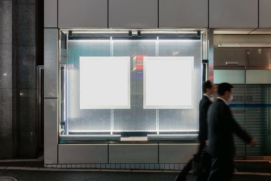 Storefront window mockup with two blank poster frames on perforated metal backdrop, urban street scene with blurred pedestrians passing by