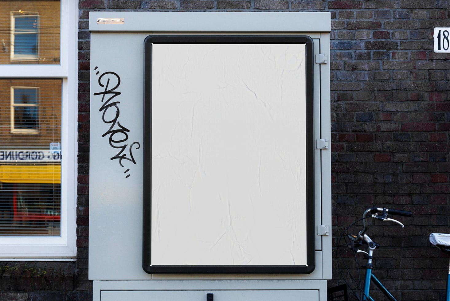 Blank storefront lightbox on brick wall with graffiti tag, bike parked nearby