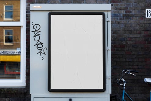 Blank storefront lightbox on brick wall with graffiti tag, bike parked nearby