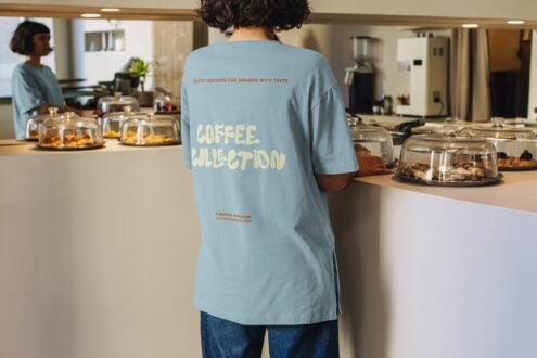 Light blue tee with coffee collection text worn in modern kitchen setting