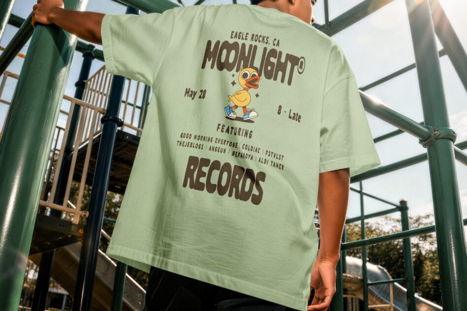 Mint green shirt back with Moonlight Records event details in brown text, outdoor metal railing behind