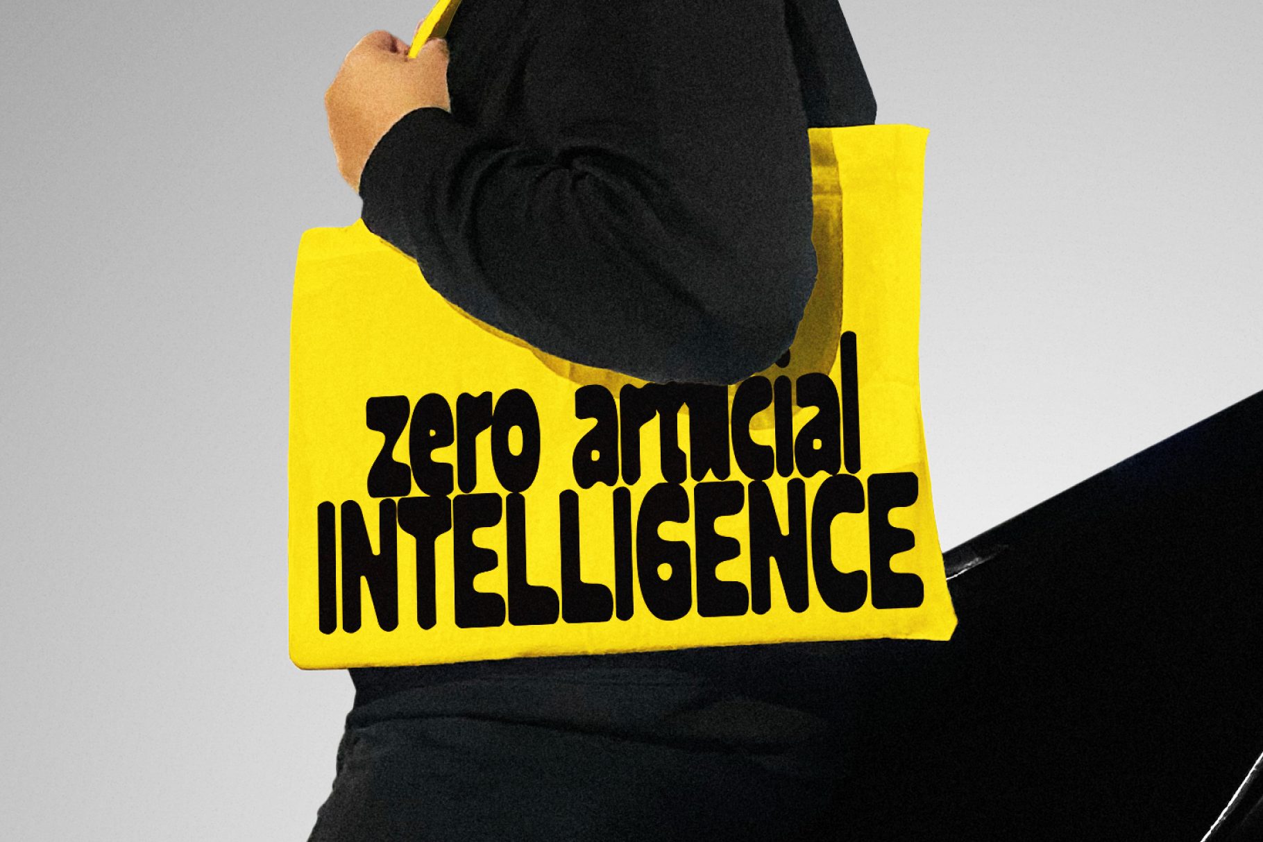 Yellow tote bag with black text saying zero artificial intelligence, held by person in dark jacket