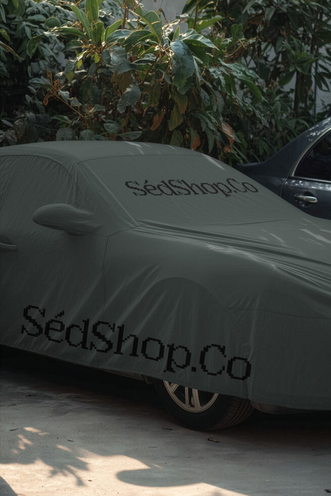 Car covered in white protective wrap with branding text visible outdoors among plants
