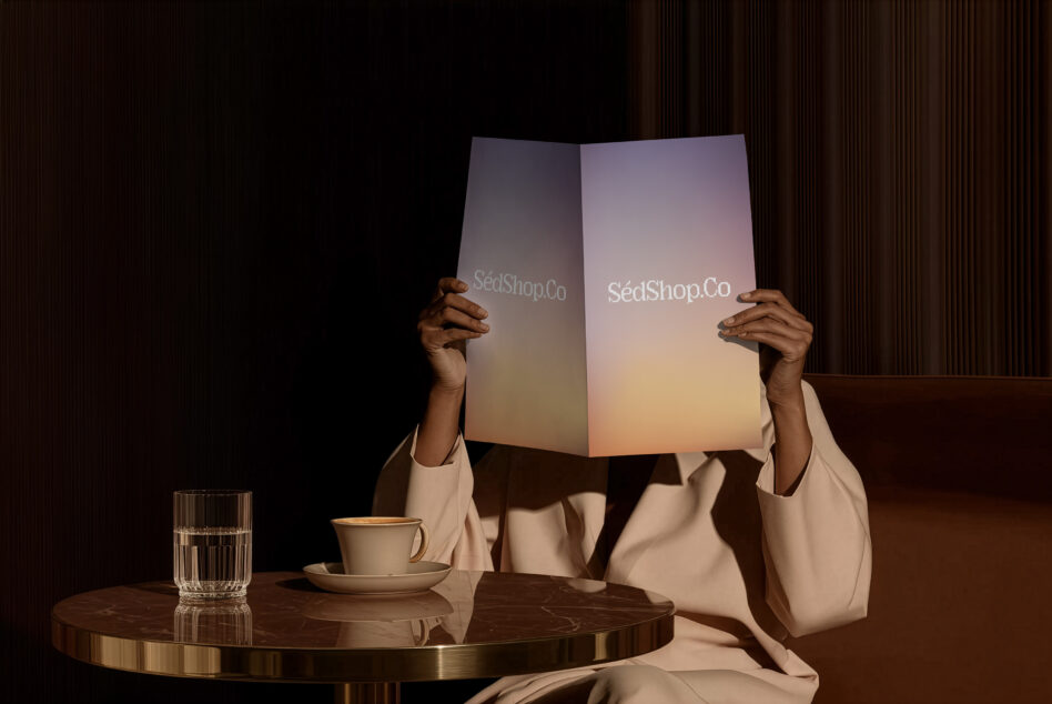 Person holding open brochure with SedShop.Co logo at modern table with coffee cup