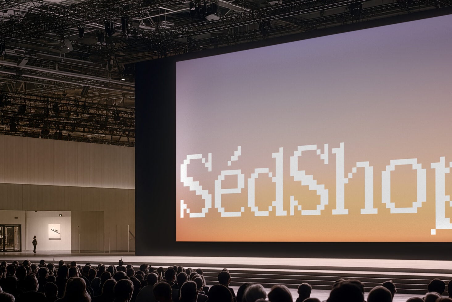Pixelated text on massive conference screen with warm gradient backdrop, industrial ceiling rigging visible above