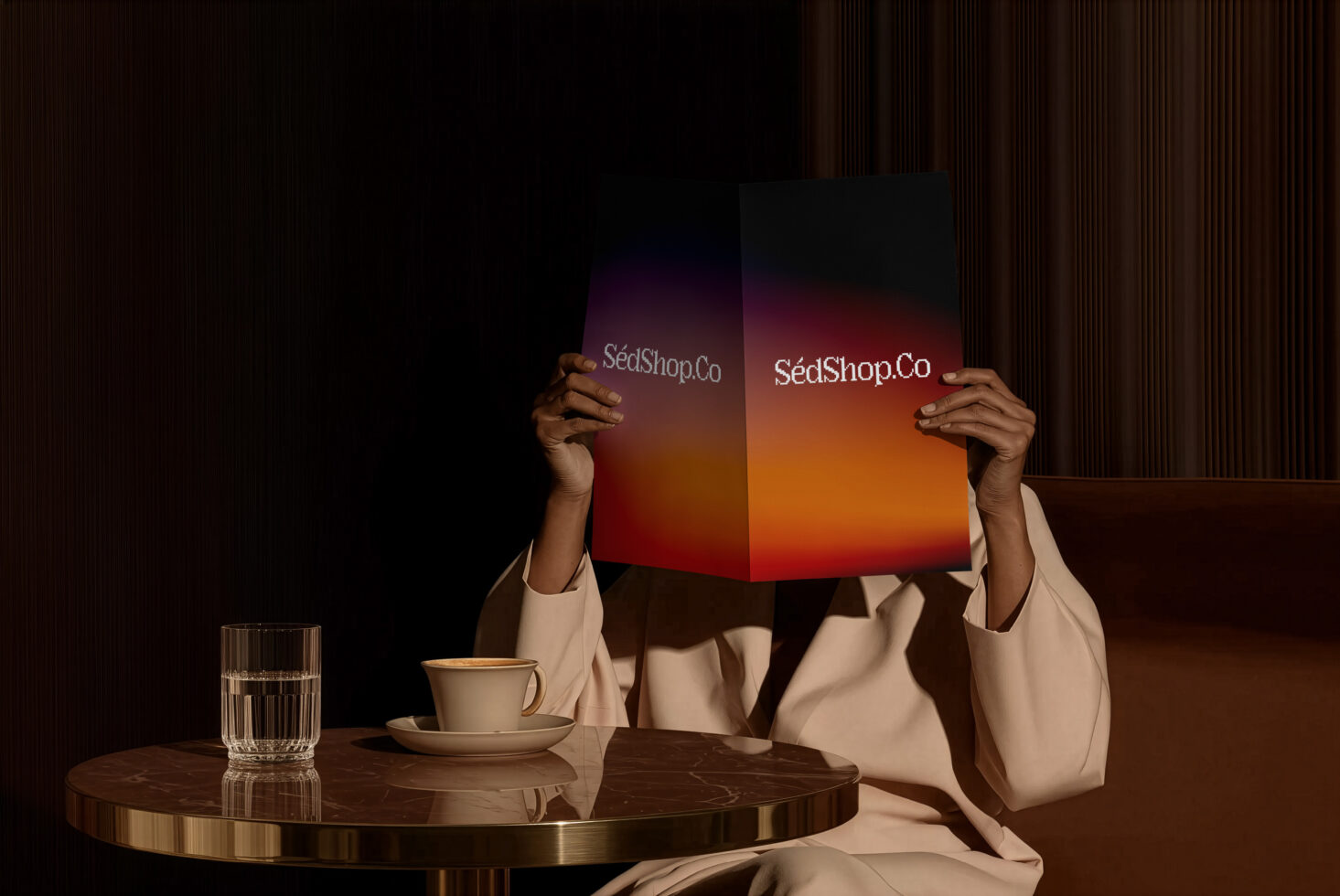 Person holding open bifold brochure with warm gradient displaying SedShop.Co logo at cafe table
