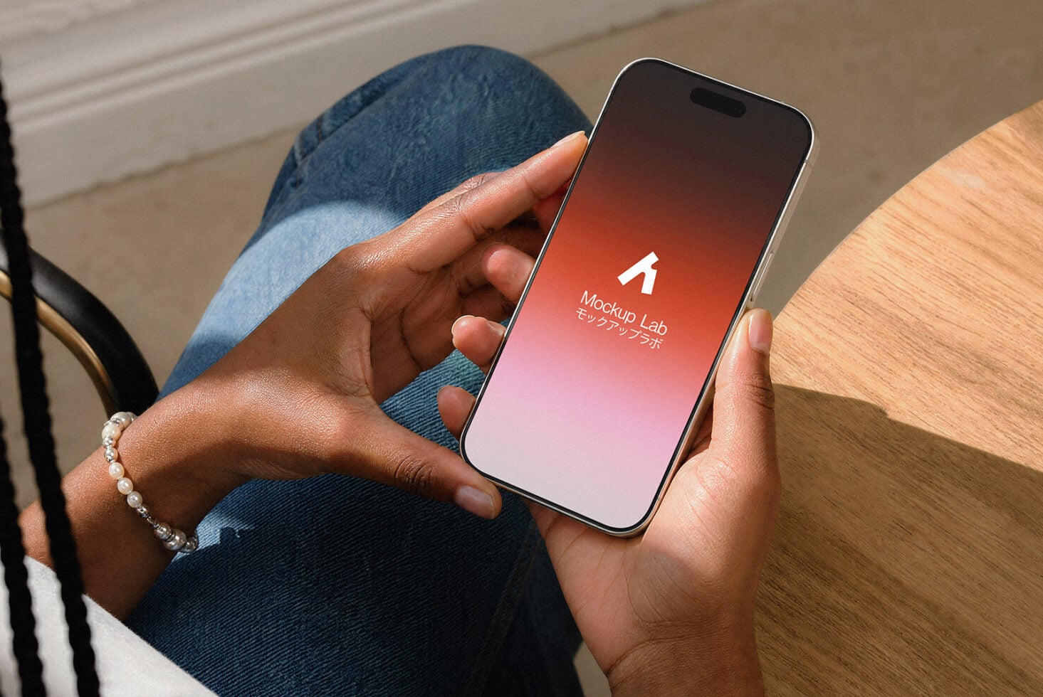 Hand holding iPhone with red gradient splash screen, sitting on wooden table with denim jeans visible