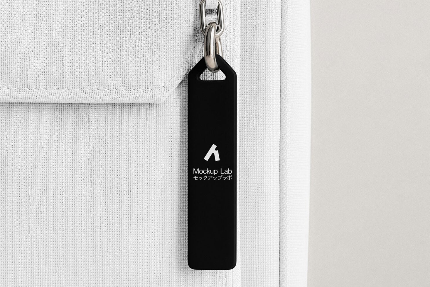 Black zipper tag on white canvas bag showing Mockup Lab branding with metal chain hook