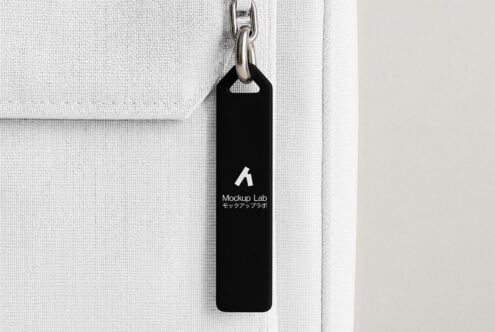Black zipper tag on white canvas bag showing Mockup Lab branding with metal chain hook