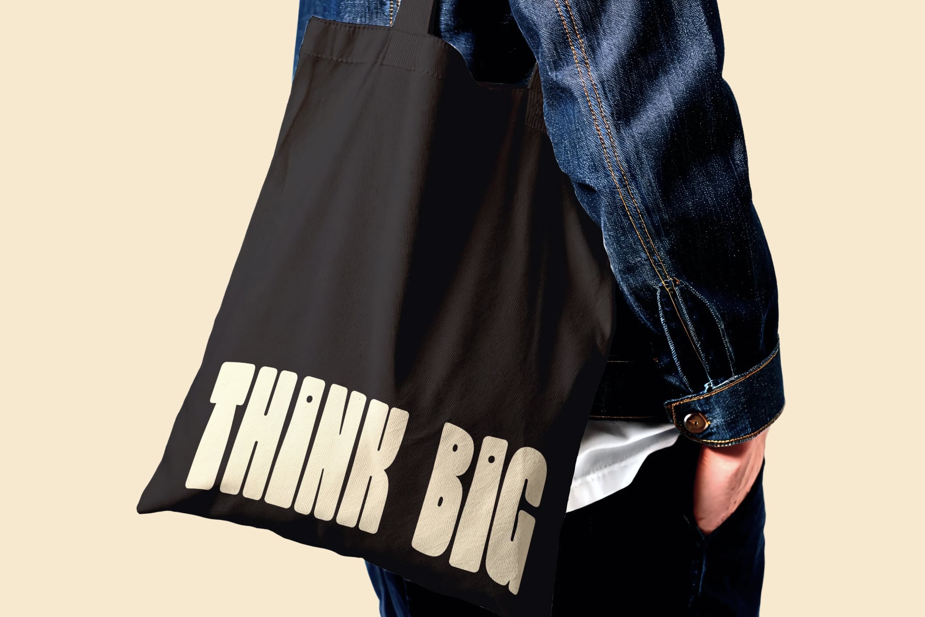 Black tote bag with cream textured lettering worn over denim jacket