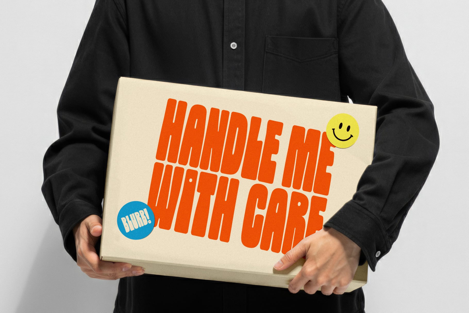 Person in black shirt holding cream box with bold orange text saying "handle me with care" plus yellow smiley face sticker