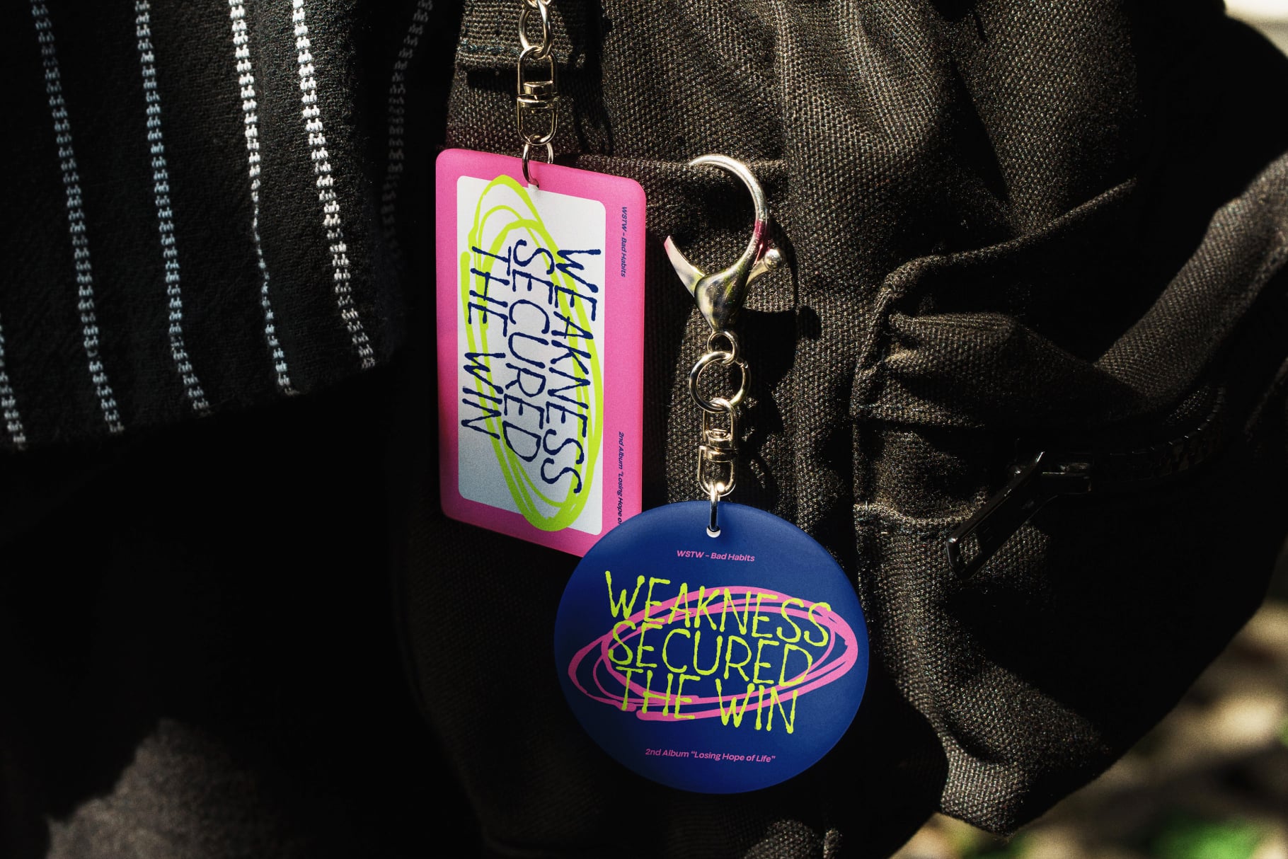 Neon keychains with bold typography hanging from dark textured backpack straps