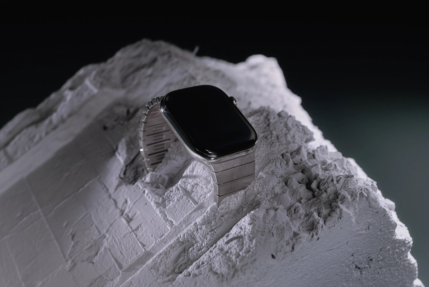 Smartwatch with silver metal band sitting on textured white plaster rock against dark background
