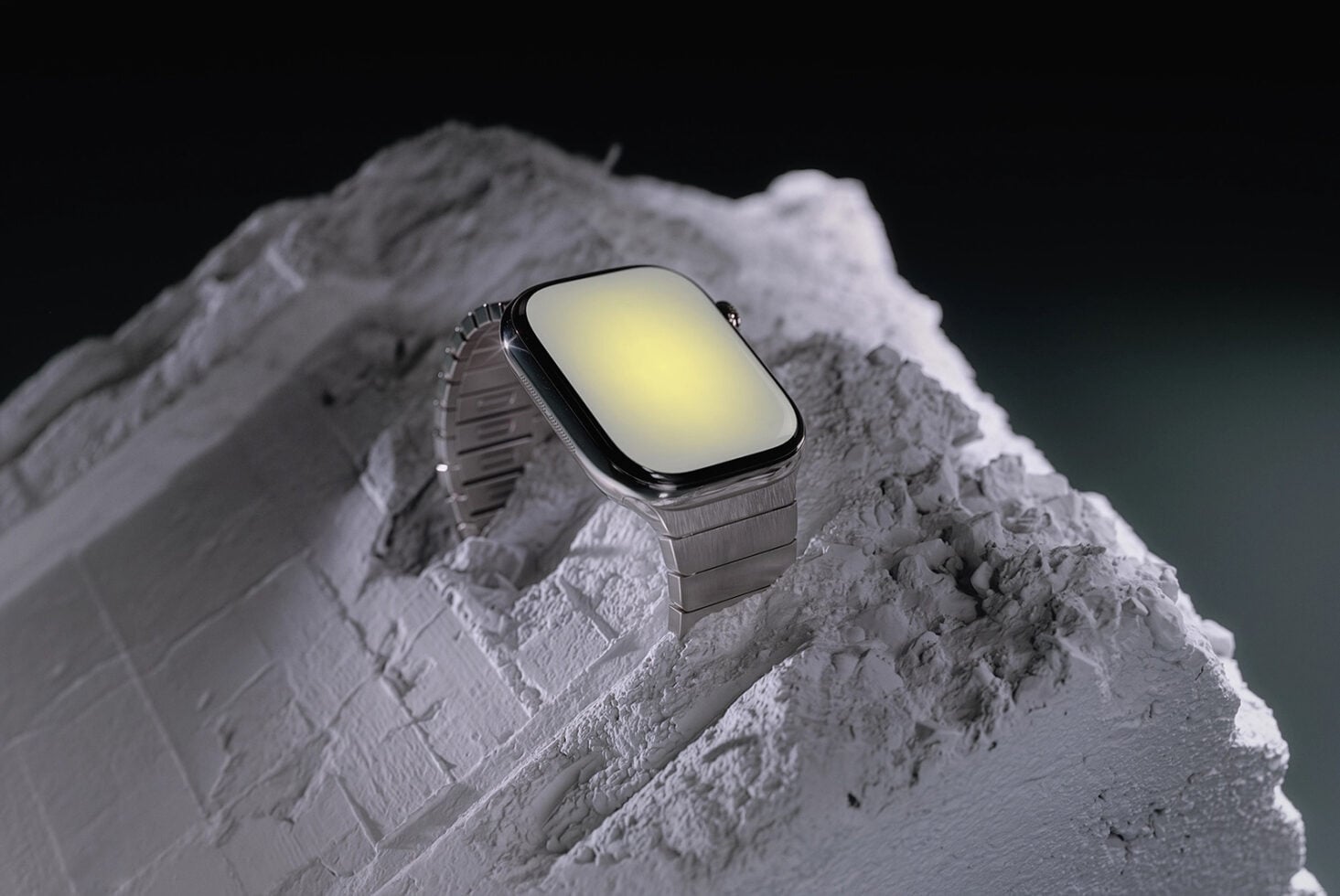 Smartwatch with square face sitting on textured white rock against dark background