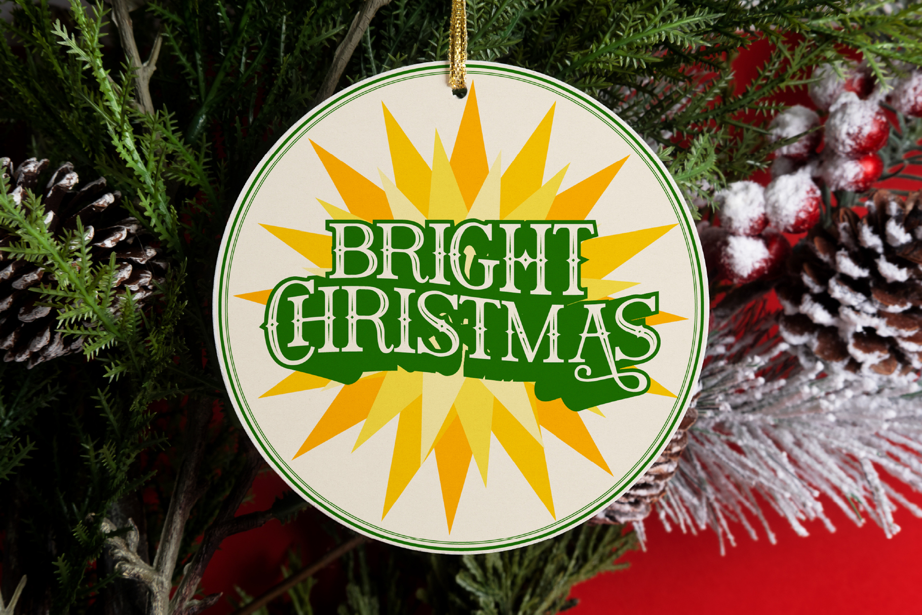 Bright Christmas ornament with yellow sunburst, green text, hanging in evergreen branches with red berries