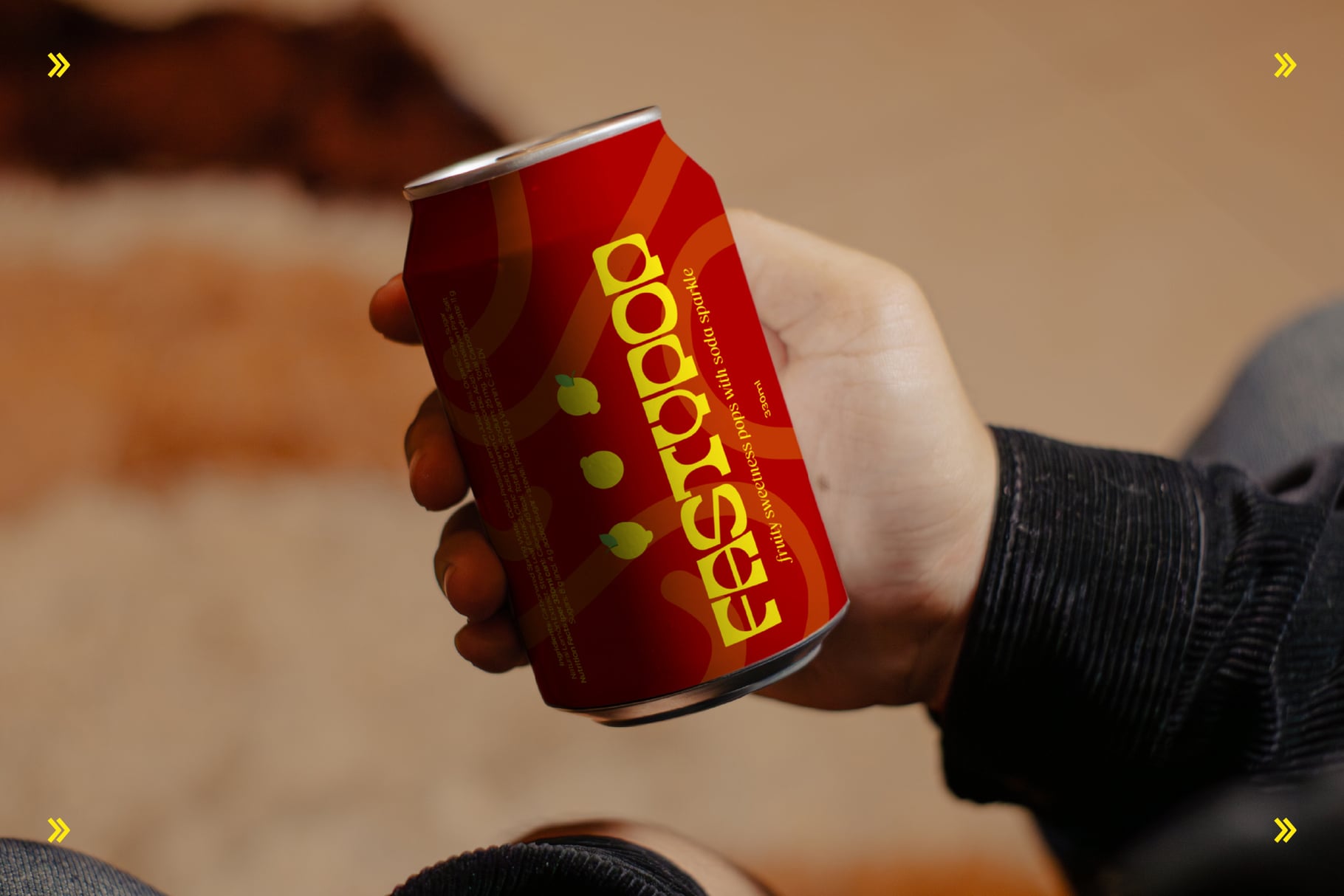 Hand holding red beverage can with yellow logo against warm blurred background