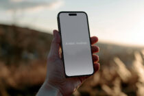 Hand holding black iPhone with gray screen outdoors at sunset