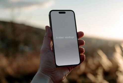 Hand holding black iPhone with gray screen outdoors at sunset