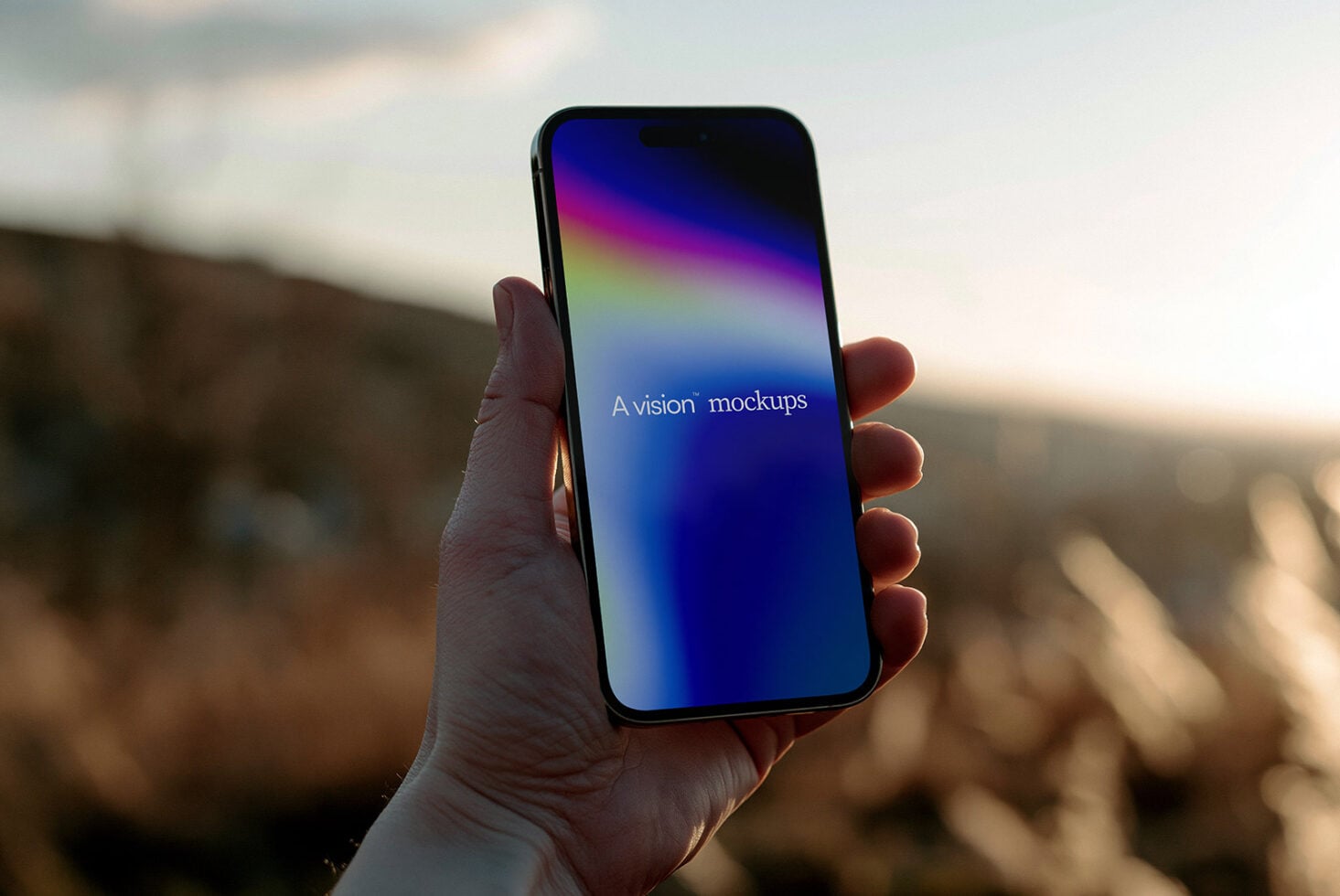 Hand holding black iPhone with colorful gradient display against blurred outdoor landscape background