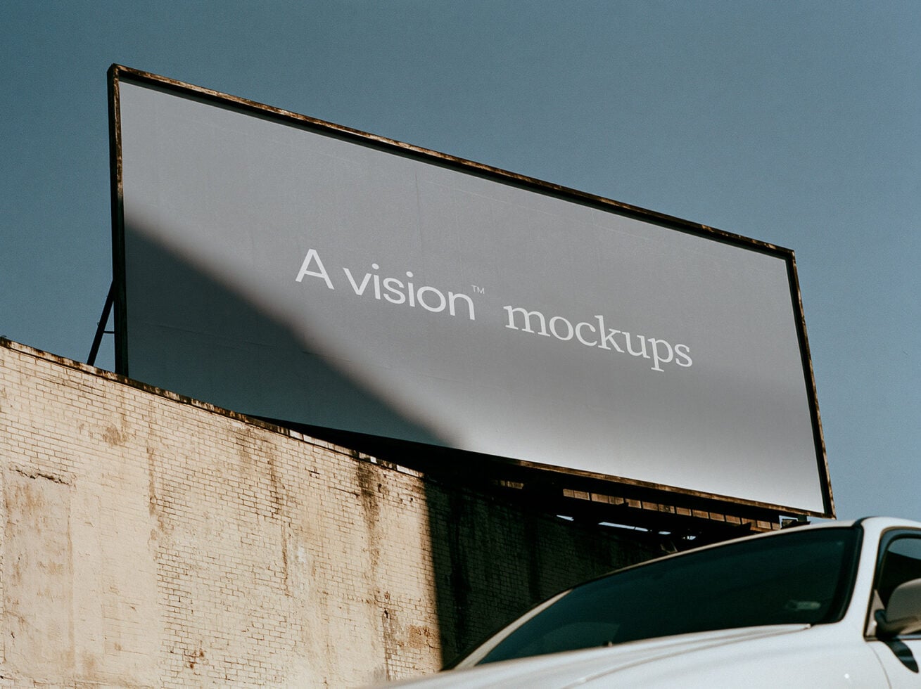 Weathered billboard with white text on gray surface, mounted on brick building under blue sky with truck below
