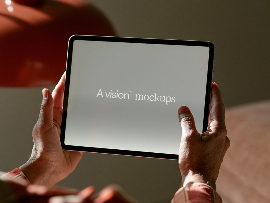 Hands holding tablet displaying "A vision mockups" text with warm studio lighting