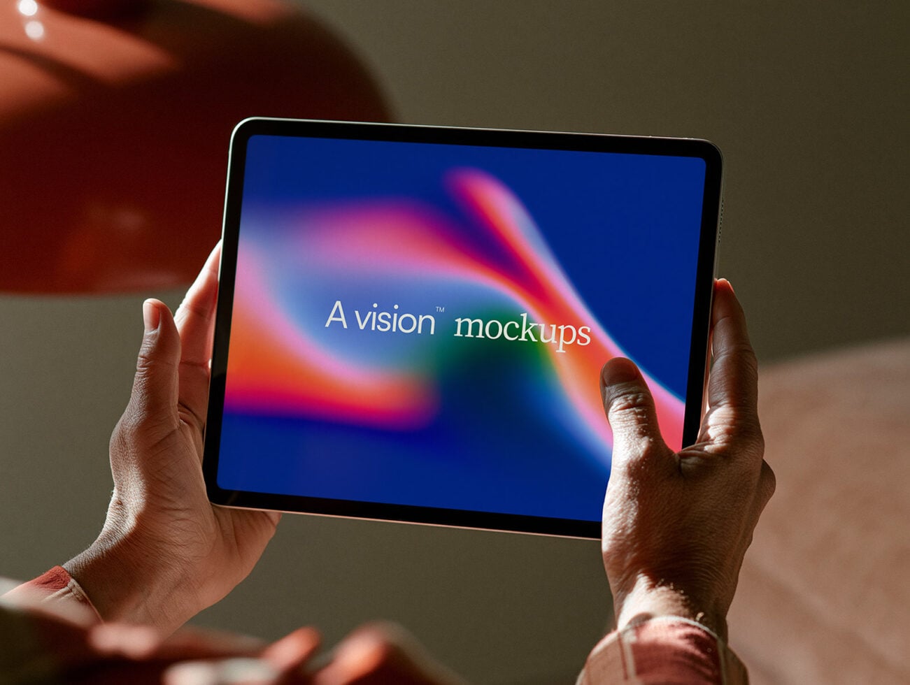 Hands holding tablet displaying colorful gradient background with "A vision mockups" text overlay in warm lighting