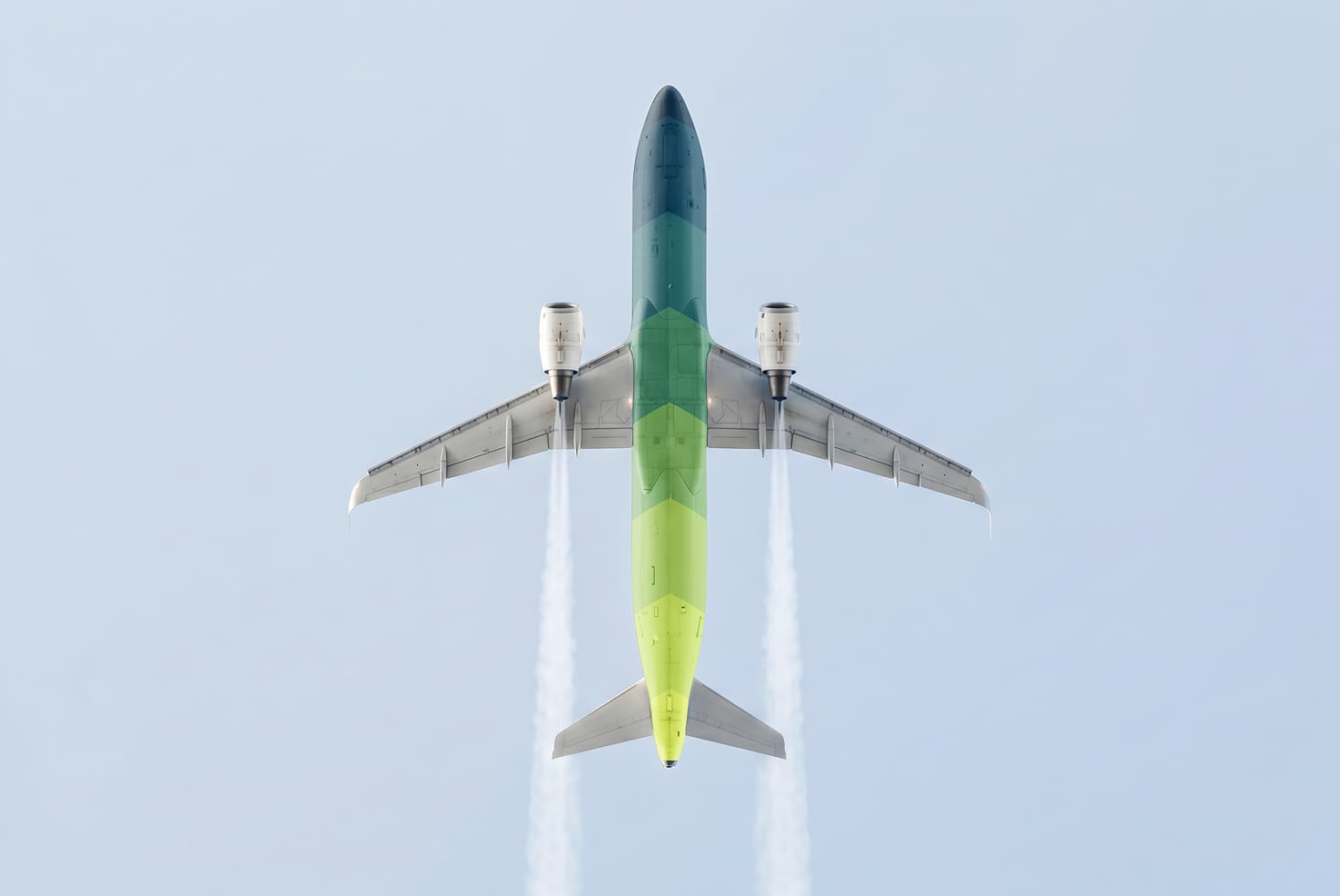 Overhead shot of commercial airplane in flight with green gradient fuselage against pale blue sky