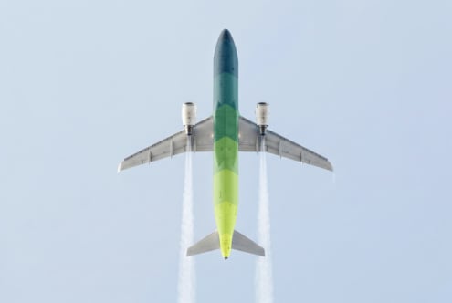 Overhead shot of commercial airplane in flight with green gradient fuselage against pale blue sky