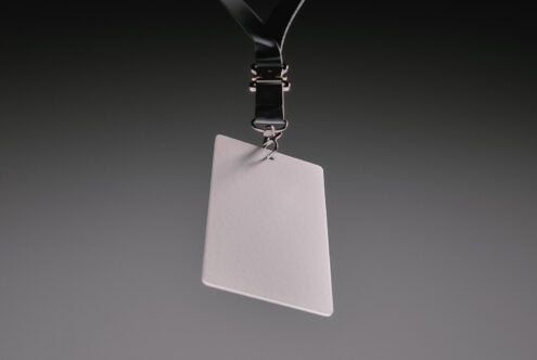 Blank ID badge hanging from black lanyard with metal clip on gray background