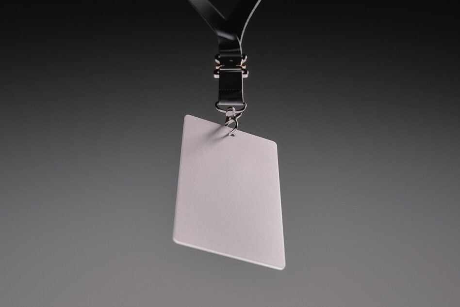 Blank ID badge hanging from black lanyard with metal clip on gray background