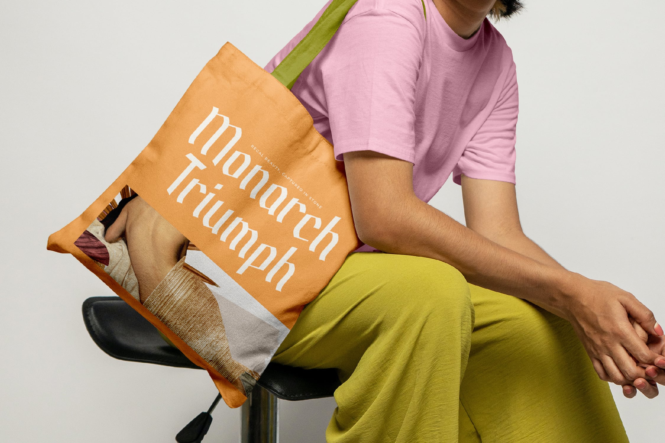 Person holding gold tote bag with "Monarch Triumph" text, wearing pink shirt, lime pants