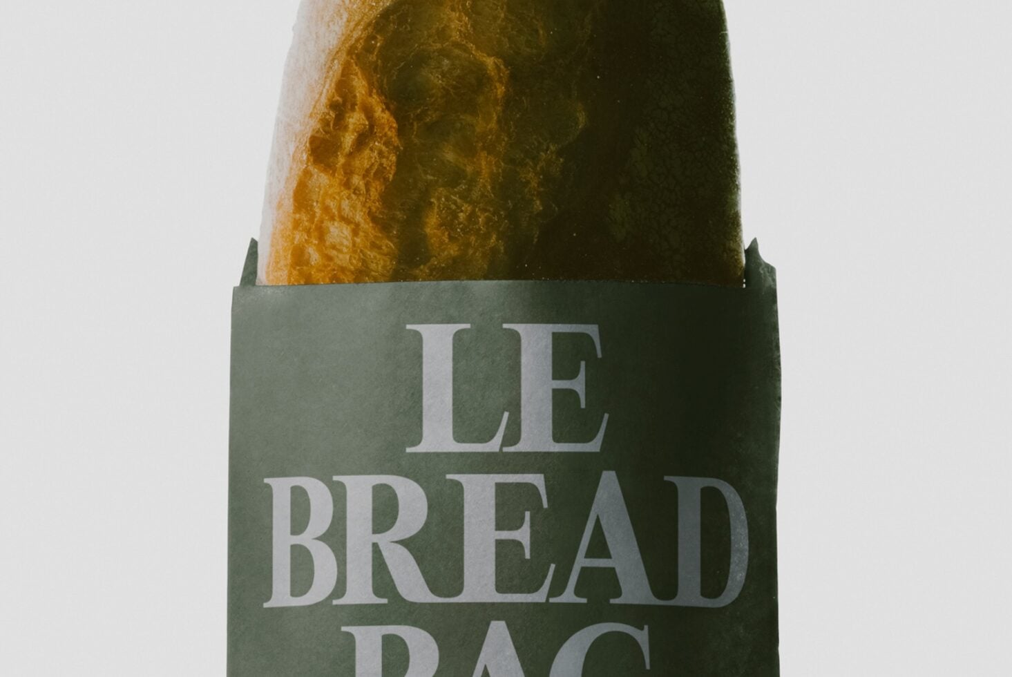 Crusty artisan bread loaf in kraft paper wrapper with sage green label showing serif typography