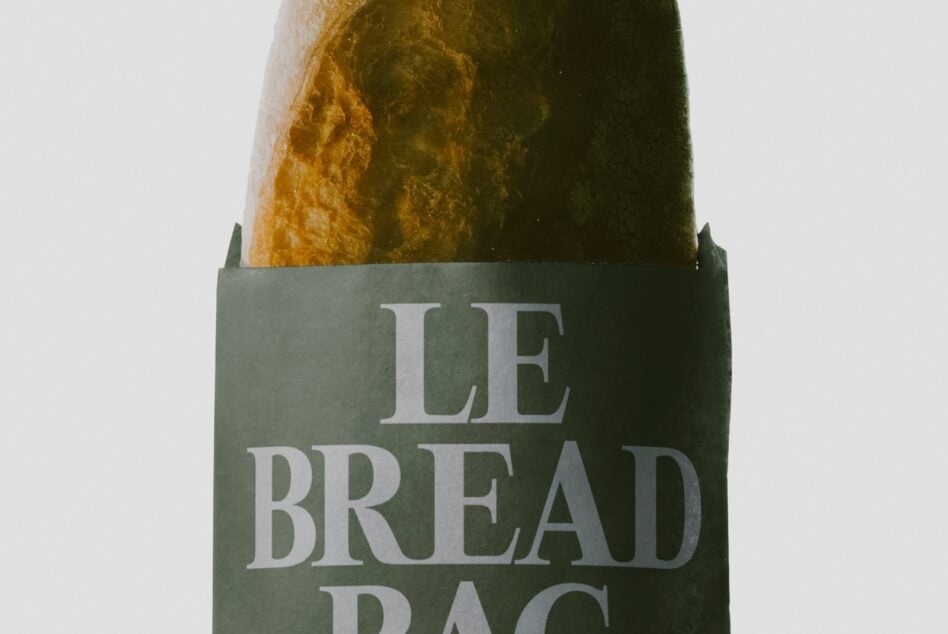 Crusty artisan bread loaf in kraft paper wrapper with sage green label showing serif typography