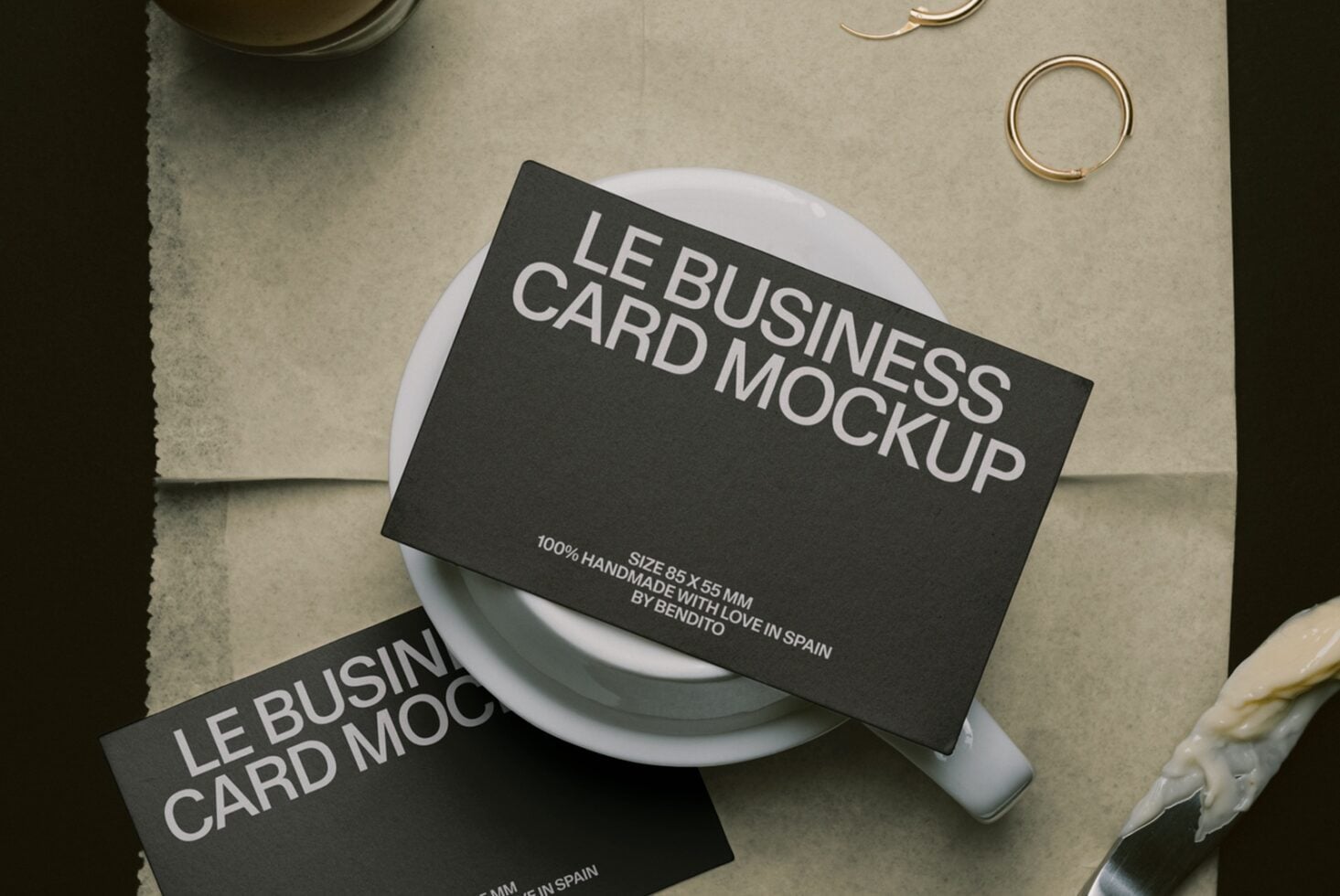 Black business cards draped on white ceramic cup with gold rings on neutral linen background