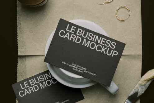 Black business cards draped on white ceramic cup with gold rings on neutral linen background