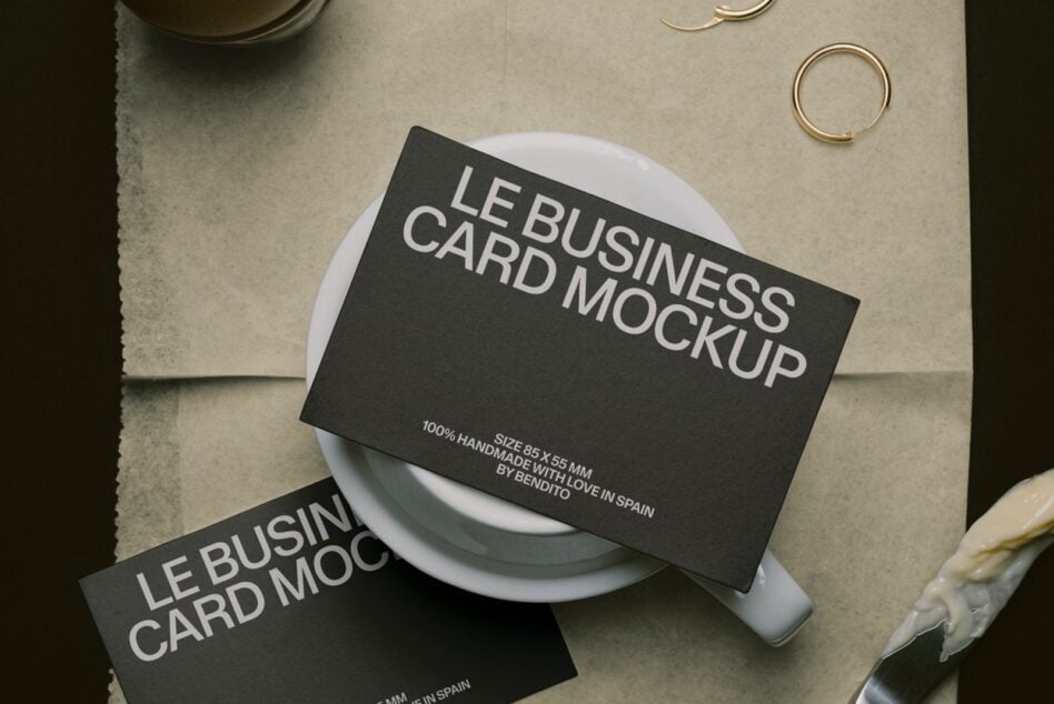 Black business cards draped on white ceramic cup with gold rings on neutral linen background