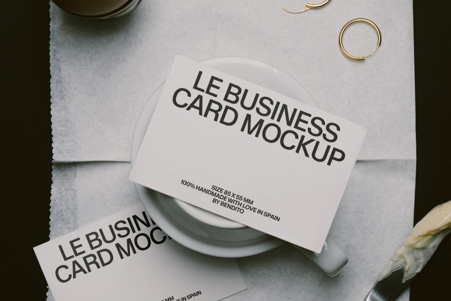 Overhead shot of business cards draped over white ceramic bowl with brass rings, neutral linen backdrop