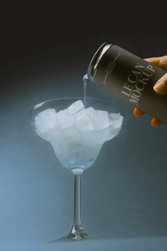 Dark bottle pouring into cocktail glass filled with ice on blue gradient background
