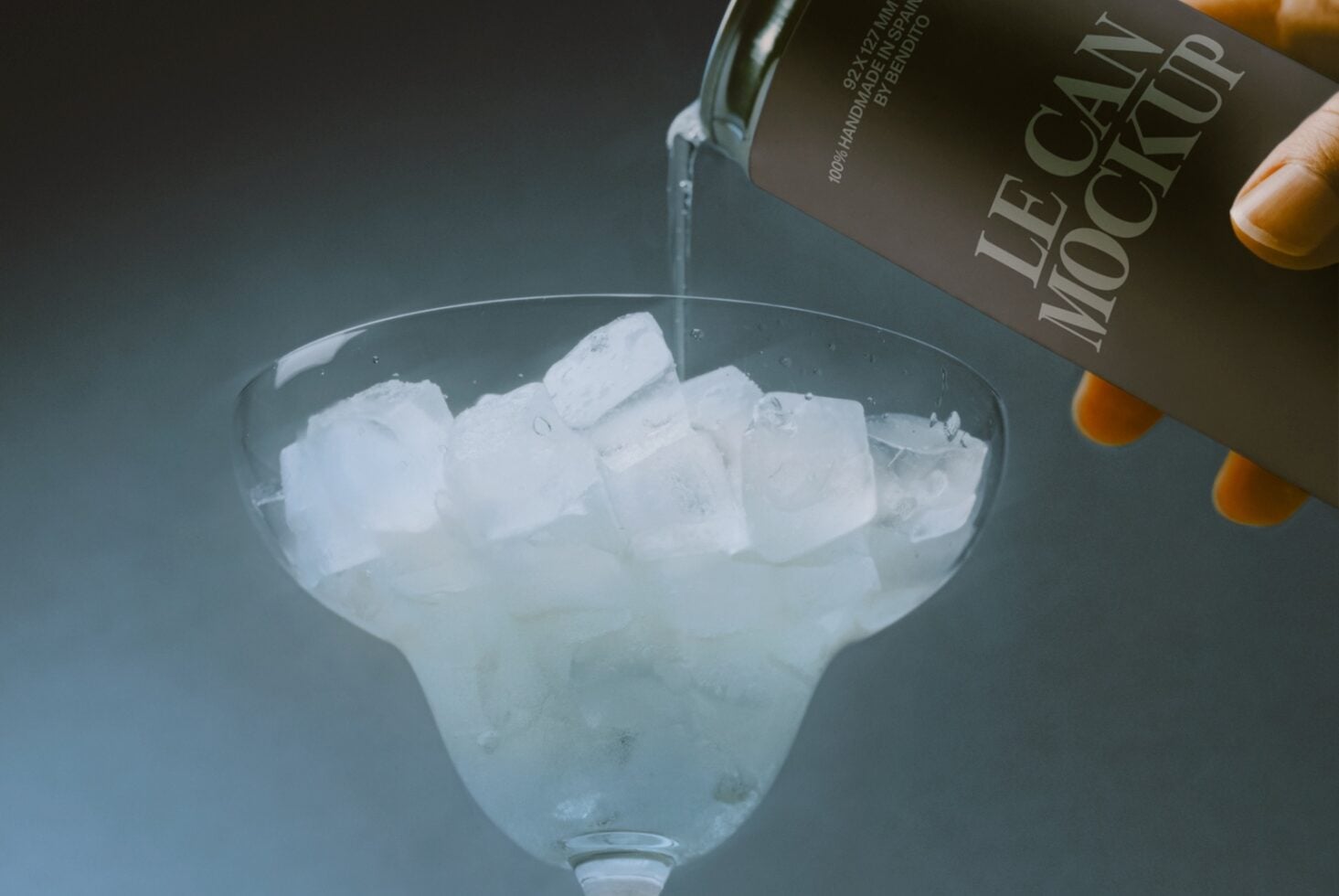 Pouring spirit into cocktail glass filled with ice cubes, dark bottle visible