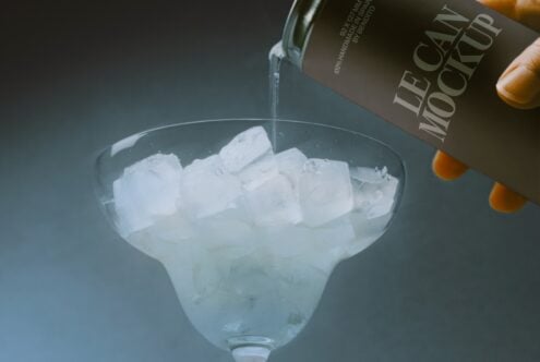 Pouring spirit into cocktail glass filled with ice cubes, dark bottle visible
