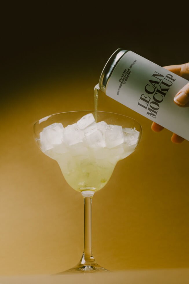 Beverage can pouring into cocktail glass with ice on golden background