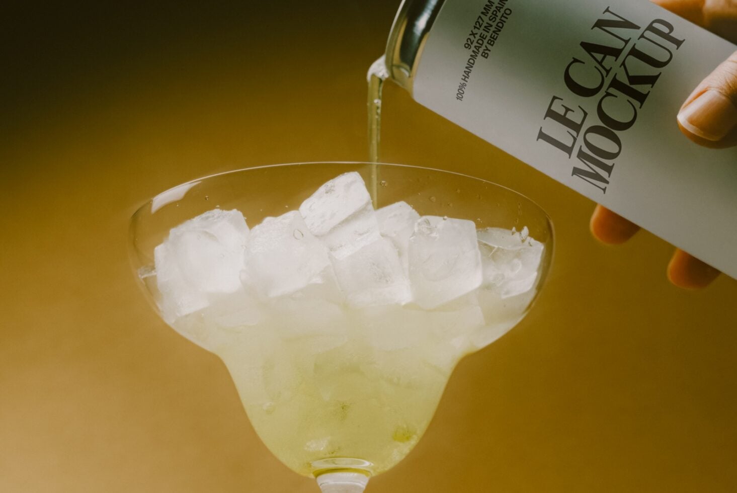 Bottle pouring pale liquor into glass with ice cubes on golden background
