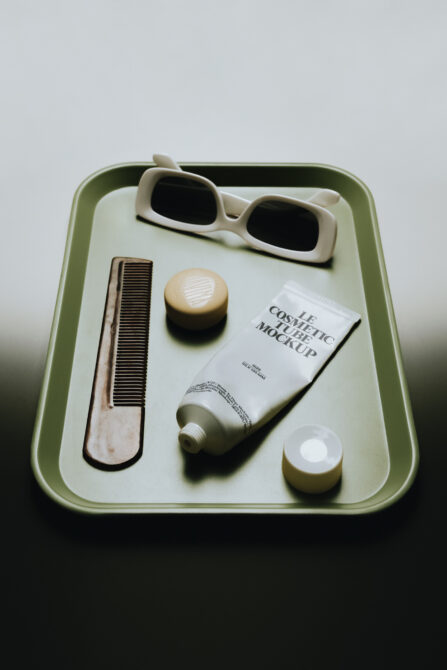 Styled flat lay of cosmetic products in sage green tray with sunglasses, comb, tube, jars