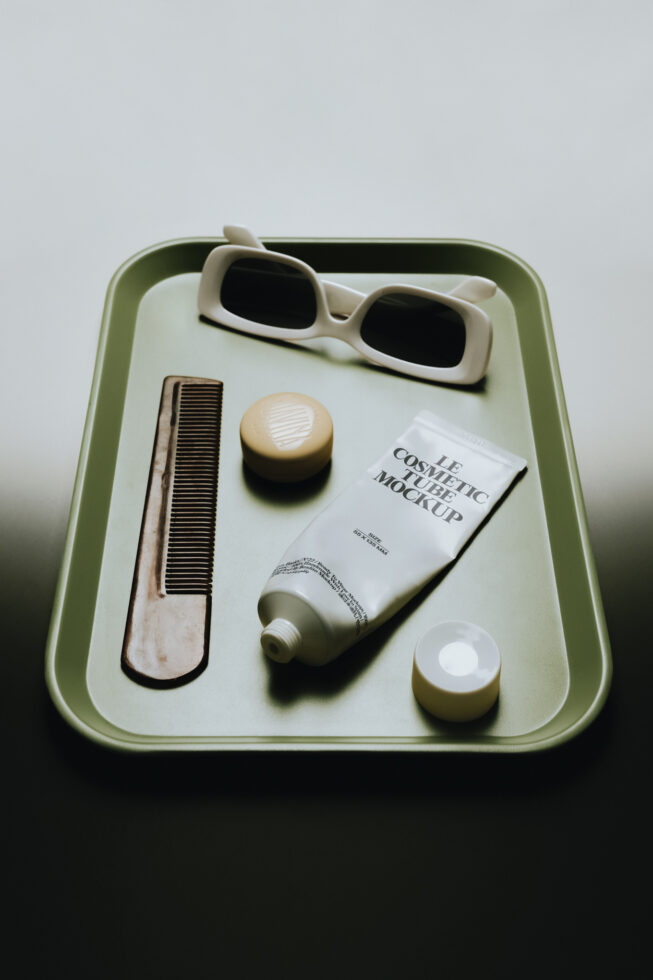 Styled flat lay of cosmetic products in sage green tray with sunglasses, comb, tube, jars