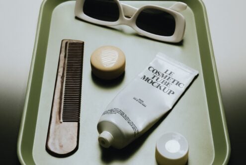 Flat lay of beauty products on sage green tray with sunglasses, wooden comb, cream jar, cosmetic tube mockup