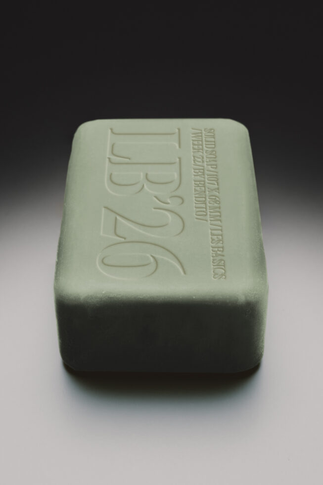 Sage green soap bar with embossed branding on top, shot against neutral background